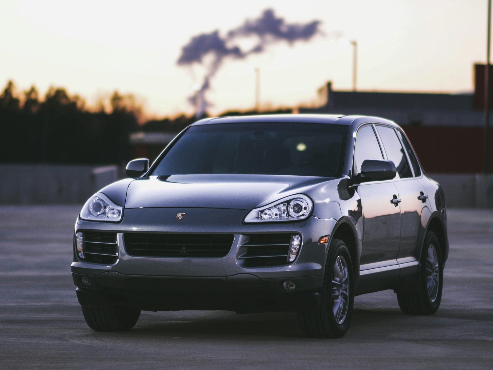 front picture of a dark grey porsche cayenne turbo gt, while being placed in a parking lot a with a small building in the distance